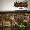 A clear glass bottle with black pour spout filled with golden olive oil alongside emperador dark marble mini versailles pattern mosaic polished tile