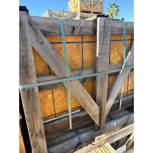 Weathered wooden crate with gold-yellow travertine Versailles pattern set, secured by teal straps