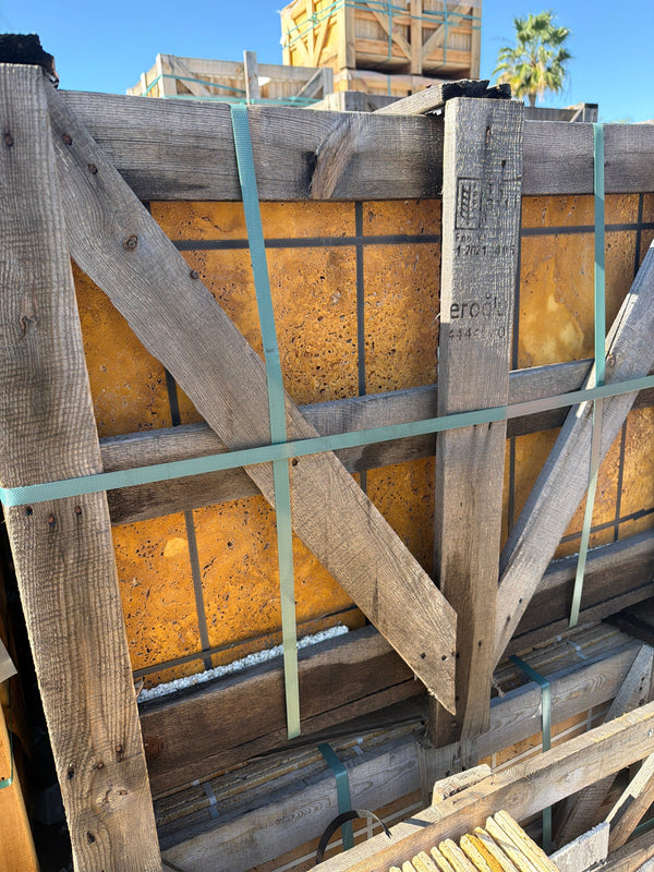 Weathered wooden crate with gold-yellow travertine Versailles pattern set, secured by teal straps
