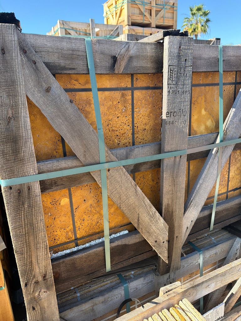 Weathered wooden crate with gold-yellow travertine Versailles pattern set, secured by teal straps