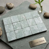 Set of sixteen ming green 3x3 tumbled marble tiles in light green with subtle veining arranged in a grid