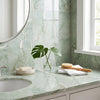 A polished ming green jade green 12x12 marble tile displayed with a clear glass vase holding a single glossy monstera leaf