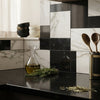 A clear glass carafe with golden olive oil and rosemary on a black countertop in modena calacatta gold and nero marquina tile set