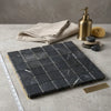 Dark gray Nero Marquina marble 2x2 tumbled mosaic tile panel with subtle white veining arranged in a grid pattern
