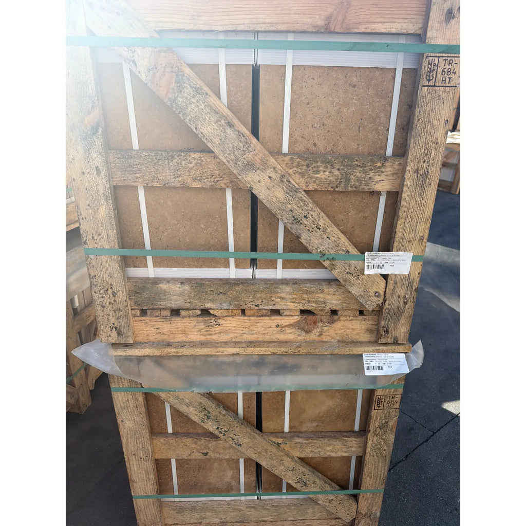 Weathered wooden pallet with diagonal crossbeams and green plastic strapping holding noce brown travertine 12x24 cross-cut filled and honed tiles