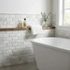 White marble subway tile wall with polished honed deep-beveled mosaic above freestanding bathtub and wooden shelf