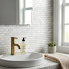 Gold-toned faucet with modern design on white ceramic sink paired with oriental white asian statuary marble mosaic
