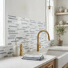 Gold-finished kitchen faucet with curved spout and single handle installed above oriental white asian statuary bamboo sticks marble mosaic