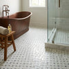 Copper bathtub with vintage-style faucet and rounded edges next to oriental white Asian statuary basketweave with blue-gray marble mosaic polished or honed