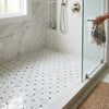 A hand holds a striped towel with fringed edges alongside oriental white asian statuary lattice marble mosaic tiles