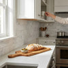 A rustic wooden cutting board with natural grain and handle holding artisan bread and green olives on oriental white asian statuary marble 3x6 tumbled