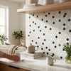 A minimalist white ceramic teapot with a matte finish on stacked cookbooks beside oriental white asian statuary penny-round marble mosaic