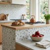 A copper teapot with a classic design and handle sits on a stovetop next to oriental white marble mosaic tiles