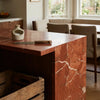 A rich reddish-orange rojo alicante marble kitchen island with swirling white veining and polished 12x12 honed surface