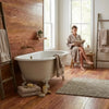 Antique white clawfoot bathtub with ornate feet and gold-tone faucet on rojo red vein-cut travertine 12x24 polished tile