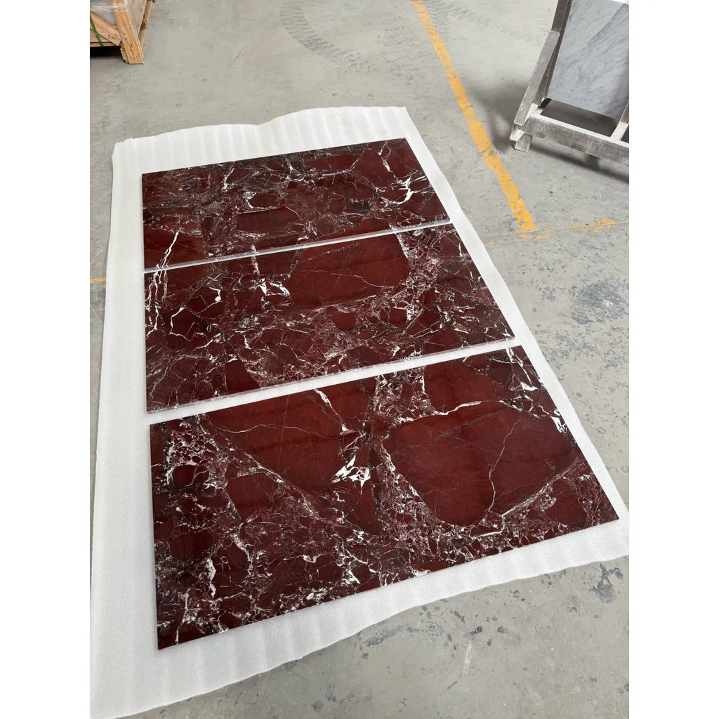 Three rectangular red rosso levanto breccia vino marble slabs with white veining on protective paper in a factory setting