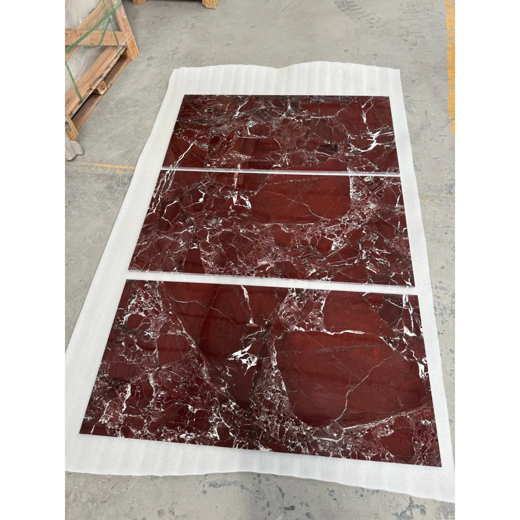 Three polished red rosso levanto marble slabs with intricate white veining wrapped in protective white material
