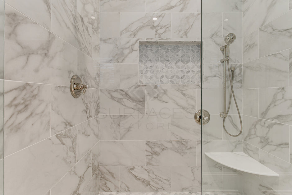 Modern shower with marble tiles, a built-in shelf with mosaic tiles, and a handheld showerhead on the right wall.