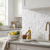 A bottle of golden olive oil with a gold cap and green olive label on a kitchen countertop beside thassos white brick mosaic marble