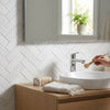 Chrome-finished single-handle bathroom faucet with sleek modern design on thassos white 1x3 herringbone mosaic marble polished or honed