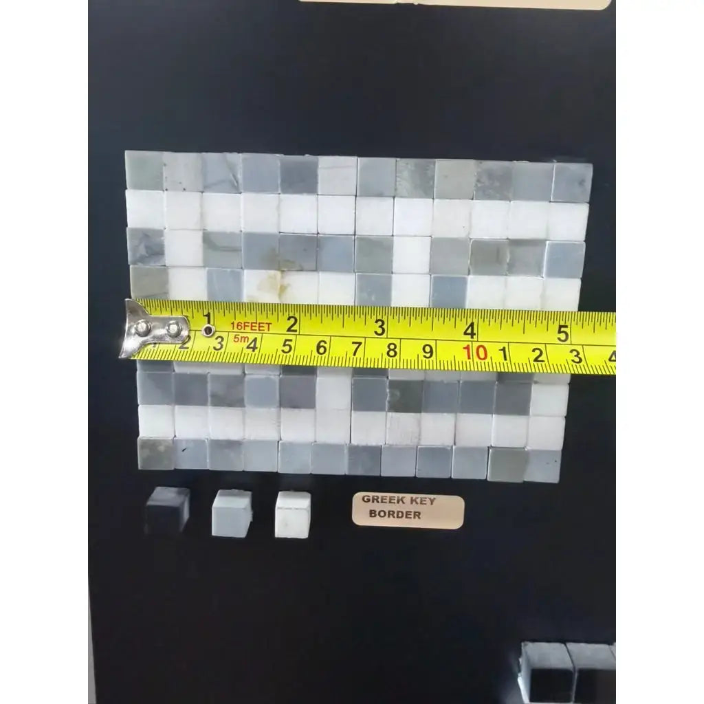 A polished or honed marble mosaic tile panel featuring a thassos white greek key border with blue-gray shades