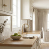A white ceramic bowl with green apples on a light wood countertop next to thassos white 3 inch hexagon mosaic marble tiles