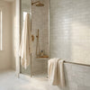Cream-colored plush towel hanging on glass shower door beside thassos white 3x6 marble tumbled tile wall