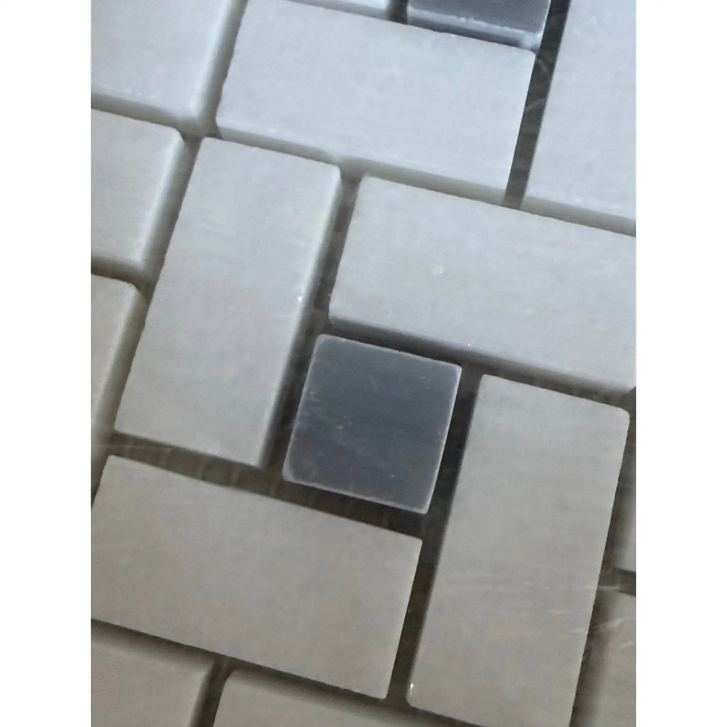 A thassos white pinwheel mosaic marble tile with a single dark gray square tile among beige rectangular tiles