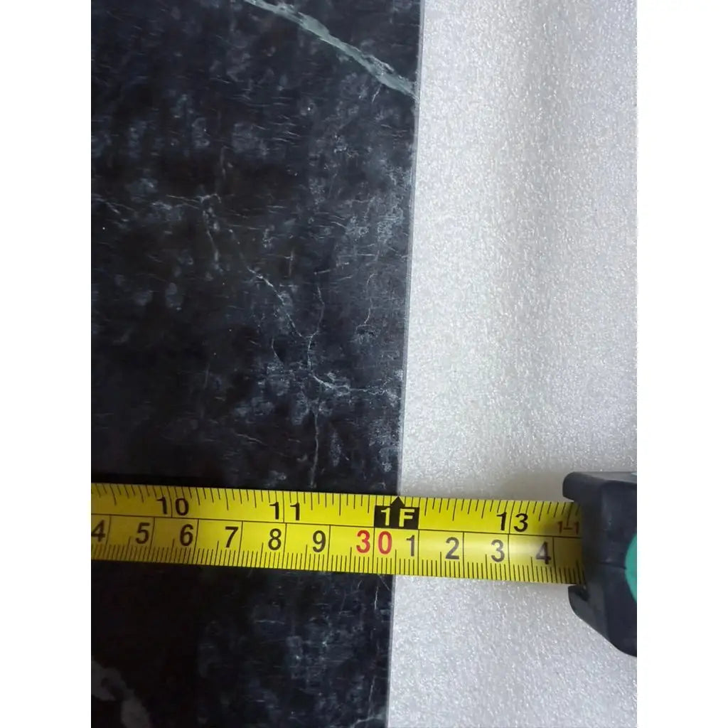 Yellow tape measure with black and green casing resting on dark marble surface next to foam padding on polished verde alpi empress green marble 12x12 tile