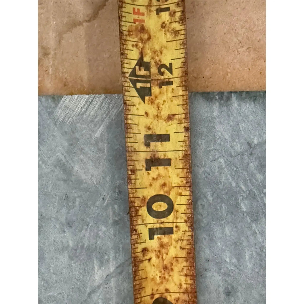 Heavily weathered yellow measuring tape in front of Verde Alpi Green Marble Tumbled product