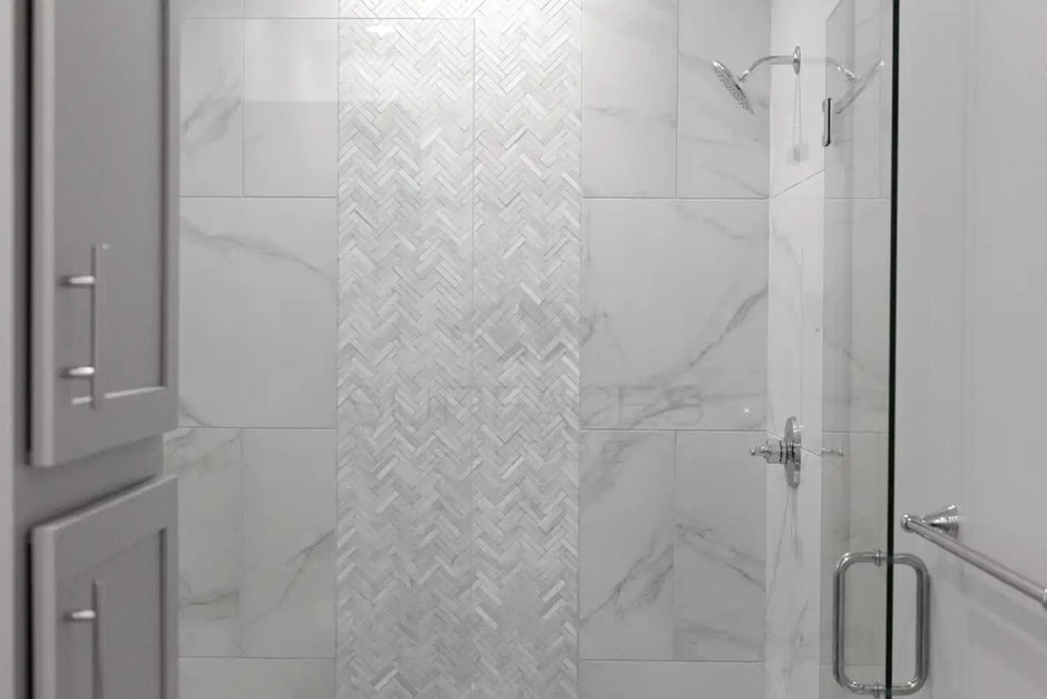 A modern shower with a glass door, white marble tiles, and a herringbone patterned accent strip in the center.