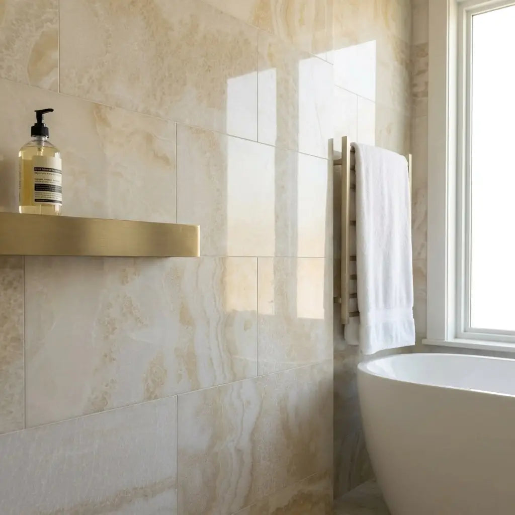 Gold-toned rectangular shelf mounted on beige marble tiled wall featuring white onyx vanilla onyx cross cut 12x24 polished marble