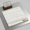 A square slab of polished white onyx vanilla onyx vein-cut marble with subtle beige veining on a metallic surface