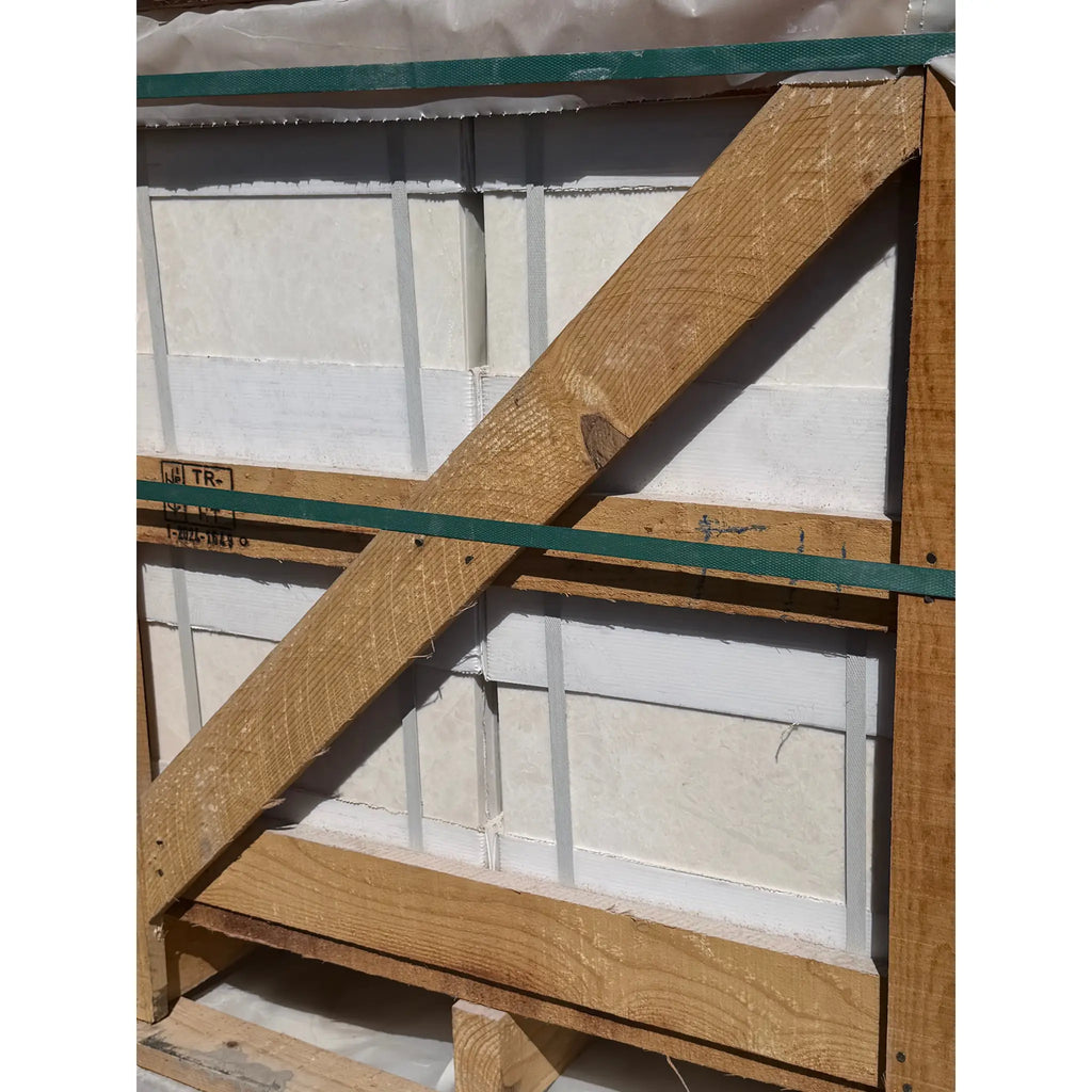 A sturdy wooden crate with diagonal crossbeams and green straps containing white pearl botticino beige marble tiles