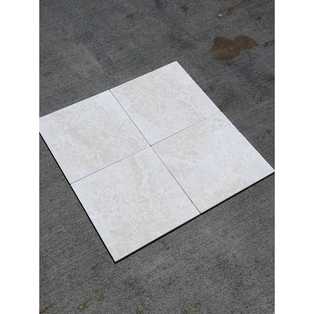 Four white pearl botticino beige marble 12x12 tumbled ceramic tiles with subtle marbled texture on dark gray surface