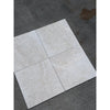 Four light gray white pearl botticino beige marble 12x12 tumbled tiles with subtle veining on dark concrete surface
