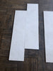Three White Pearl marble 12x24 tiles with marbled texture on wood floor