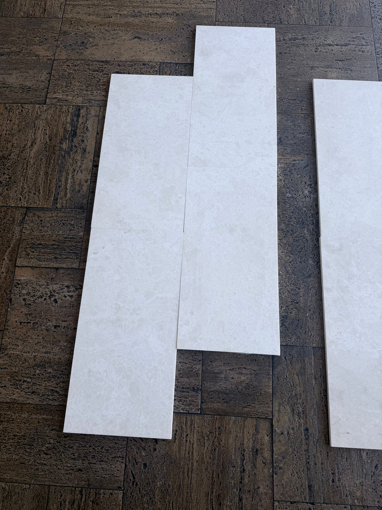 Three White Pearl marble 12x24 tiles with marbled texture on wood floor